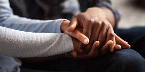 Close up black woman and man in love sitting on couch two people holding hands.